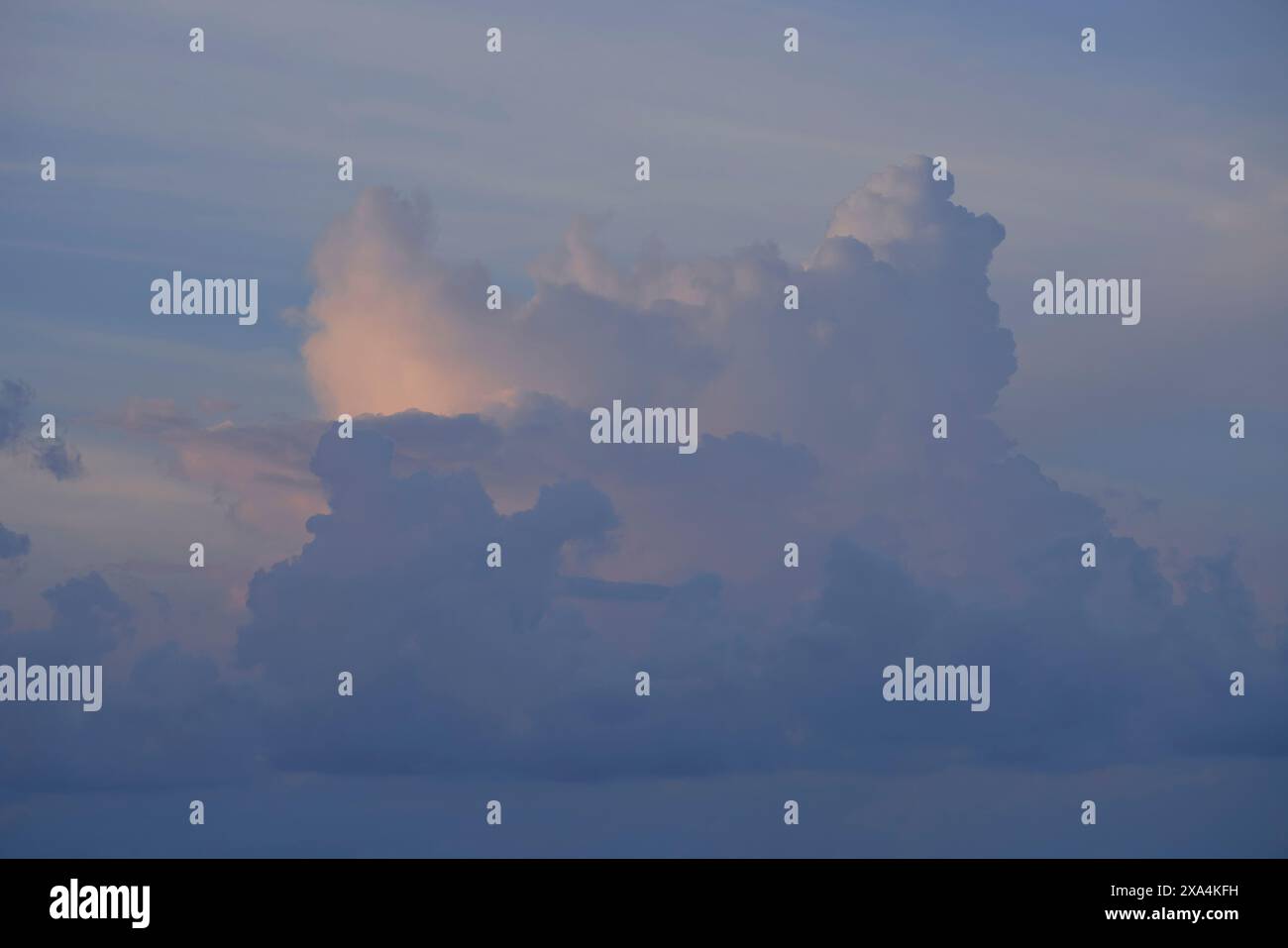Un ciel serein avec des nuages doux teintés de teintes roses du coucher ou du soleil levant. Banque D'Images