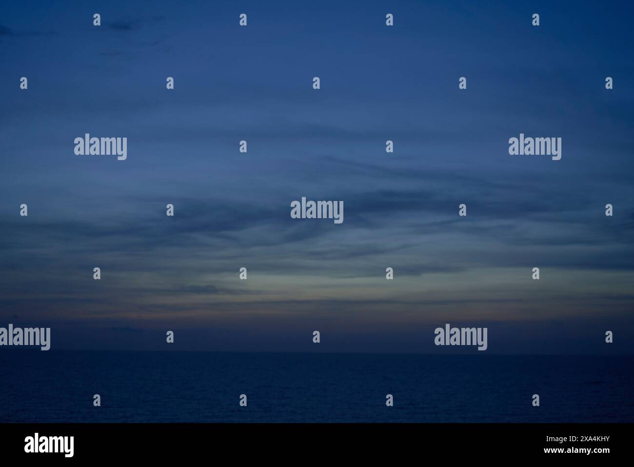 Un horizon océanique calme sous un ciel crépusculaire avec des dégradés subtils du bleu profond à l'orange près de l'horizon, et des stries de nuages au-dessus. Banque D'Images