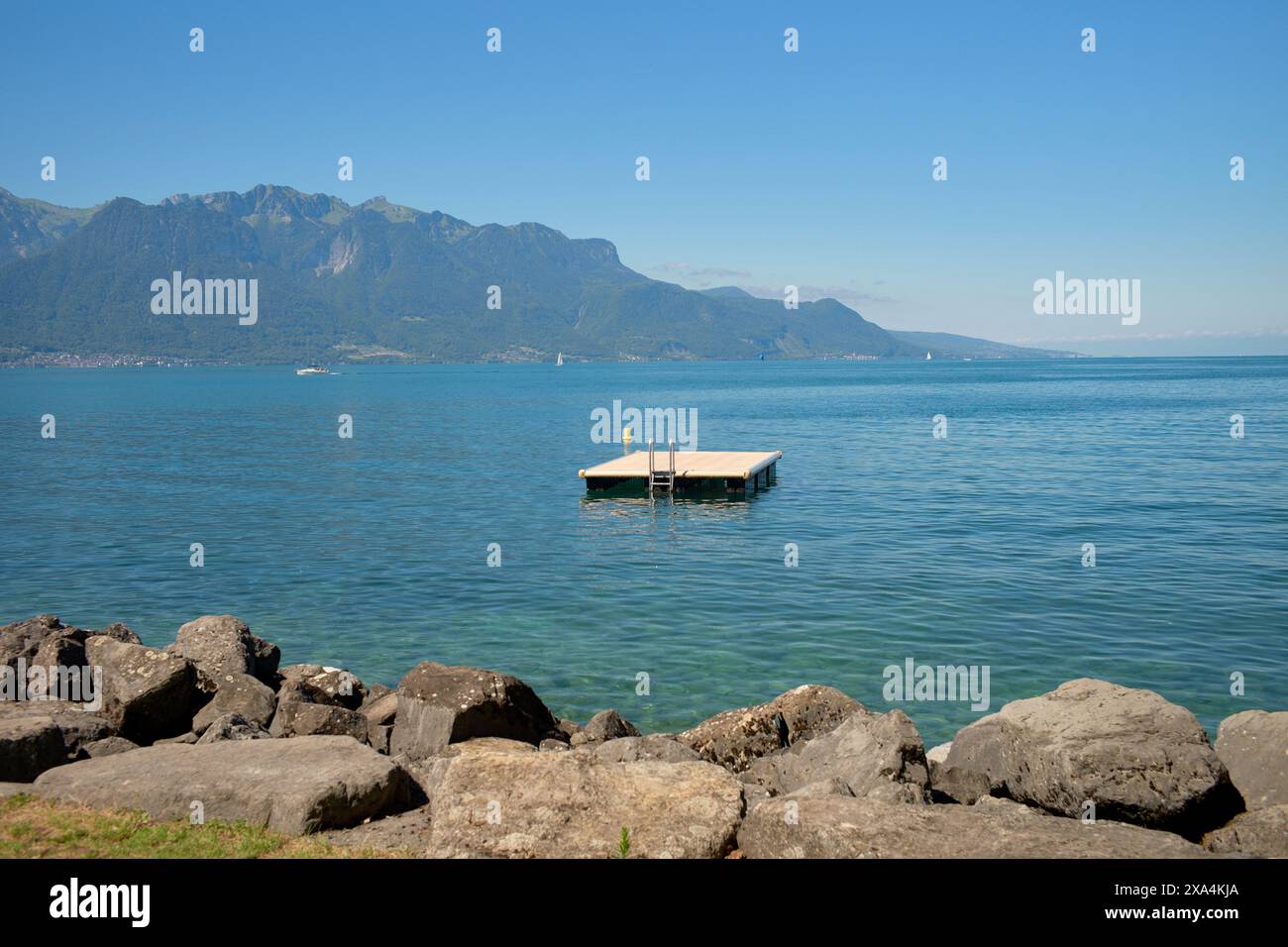 Un lac serein avec un quai flottant au centre, entouré de montagnes sous un ciel bleu clair. Banque D'Images