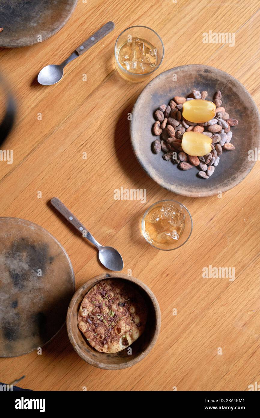Une vue aérienne d'une table rustique en bois avec deux bols de nourriture, un verre d'une boisson dorée et divers ustensiles. Banque D'Images