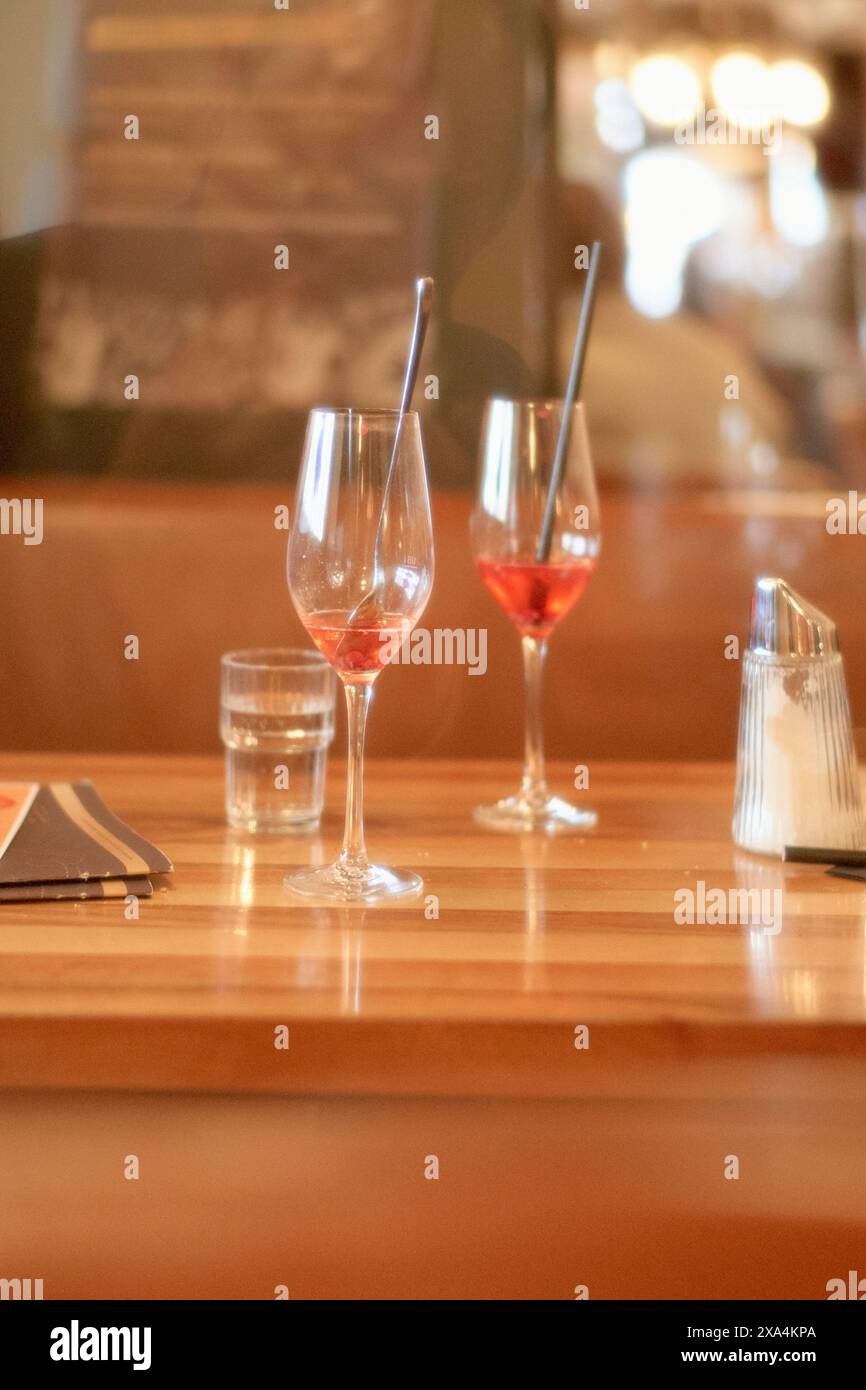 Deux verres à vin, l'un partiellement rempli de vin rose, assis sur un comptoir de bar en bois accompagné d'un verre d'eau et d'un salier, avec un fond flou suggérant un cadre de restaurant confortable. Banque D'Images