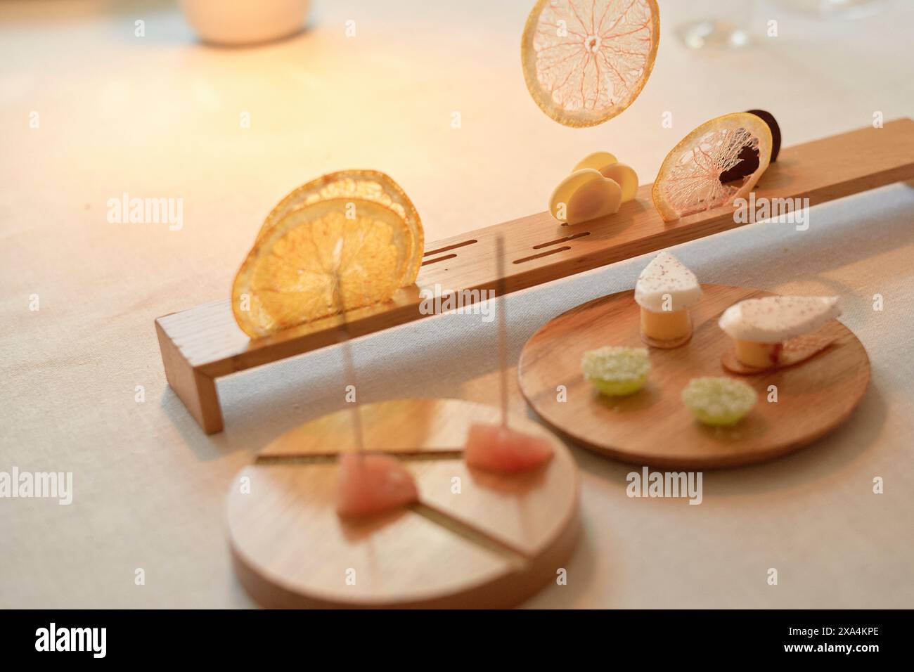 Une présentation élégante de desserts avec des agrumes finement tranchés et divers bonbons artistiquement exposés sur des stands en bois avec un éclairage chaud et diffus. Banque D'Images