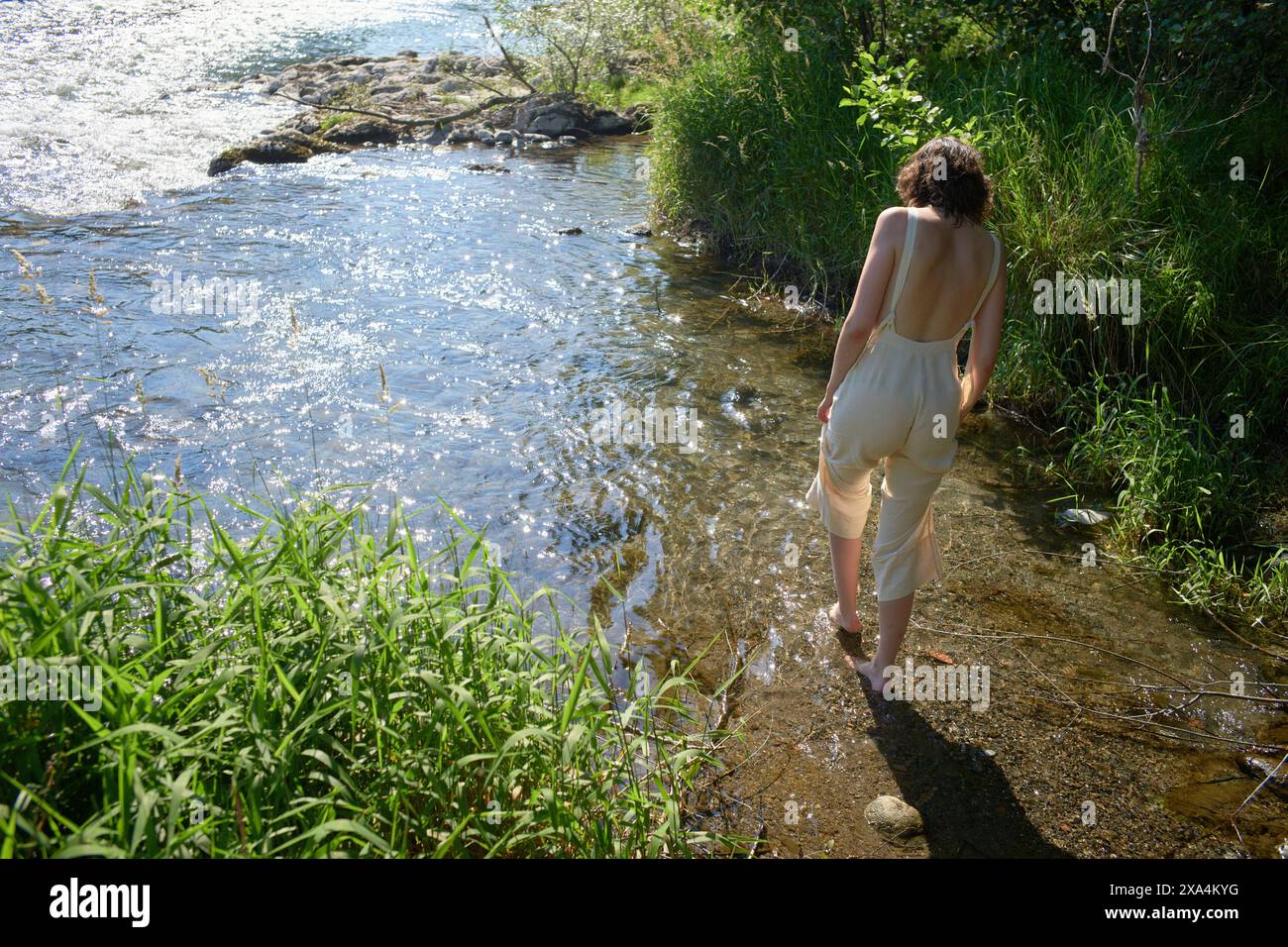 Une personne patère au bord d'une rivière ensoleillée entourée d'une végétation luxuriante. Banque D'Images