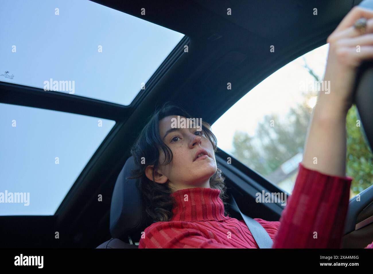 Une personne concentrée conduit une voiture avec un toit ouvrant panoramique en tenant le volant d'une main. Banque D'Images