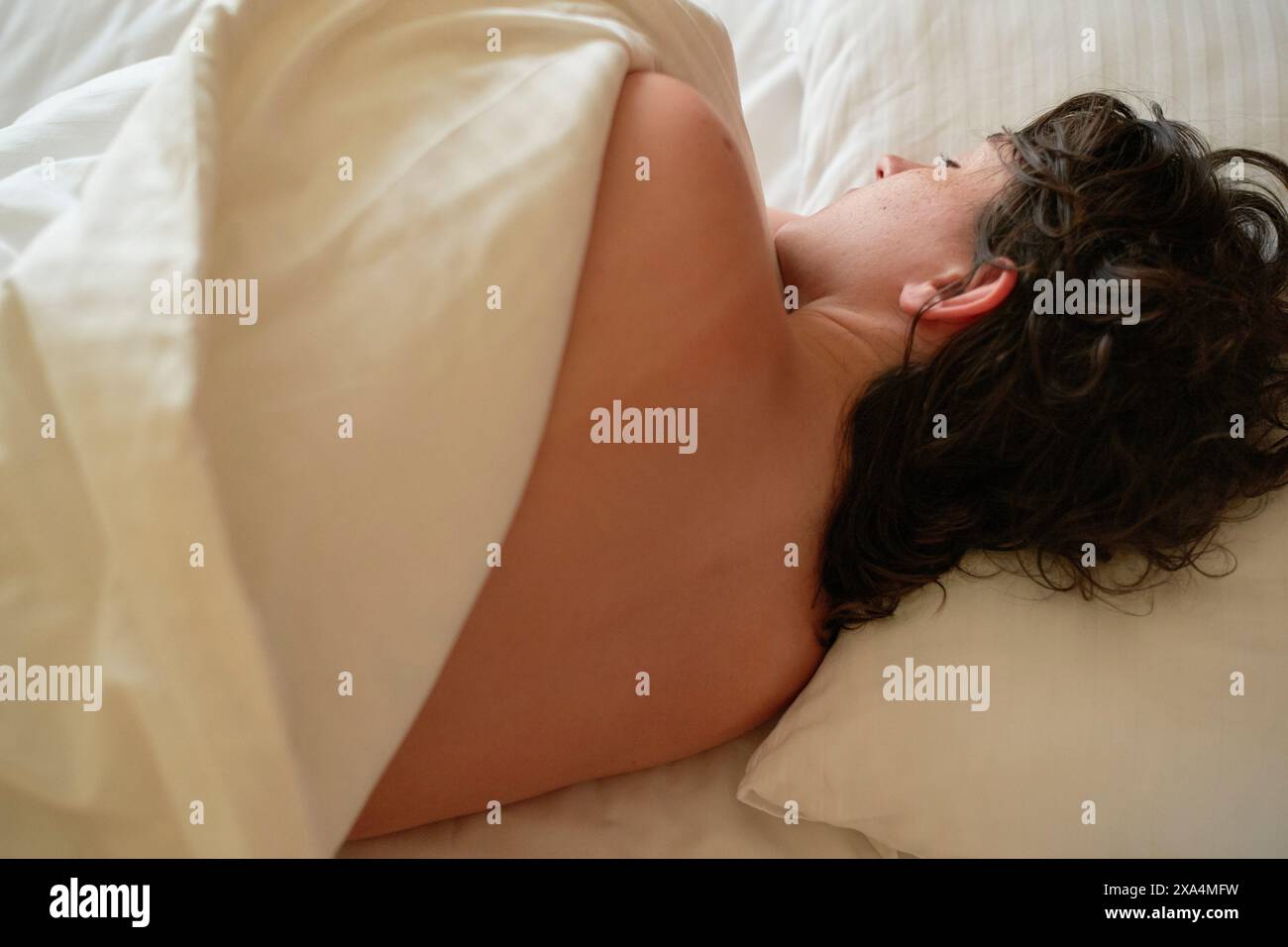 Une personne est allongée sur un lit, le visage tourné vers l'extérieur, partiellement couverte par un drap blanc. Banque D'Images