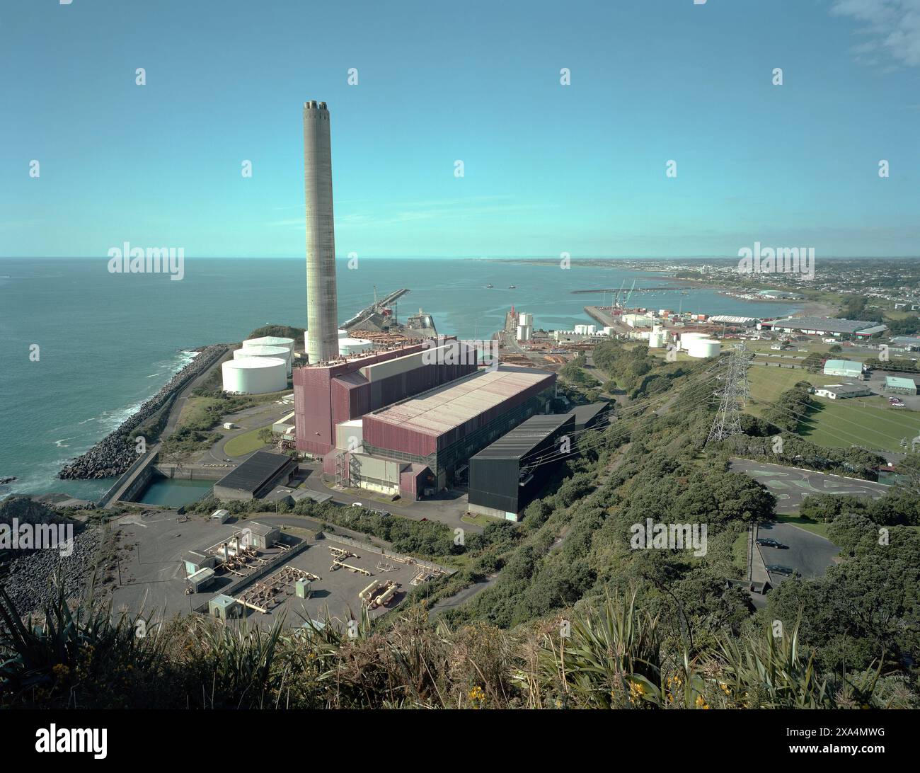 Un complexe industriel avec de grands réservoirs de stockage et une cheminée haute est positionné le long d'un littoral, New Plymouth, Nouvelle-Zélande Banque D'Images