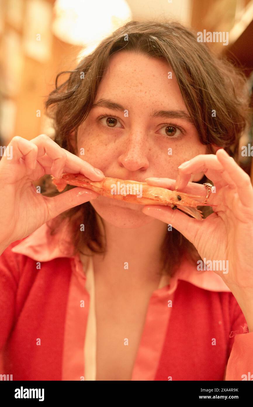Femme dans une blouse rose tenant une crevette à une table à manger. Banque D'Images