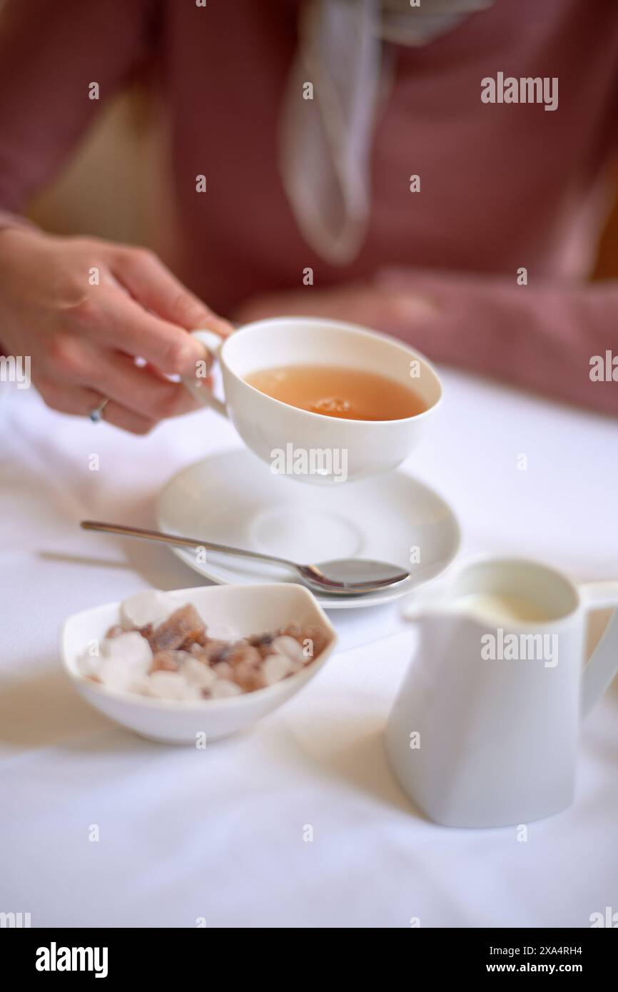 Elégante heure du thé avec une personne dégustant une tasse de thé, avec du lait et du sucre sur le côté. Banque D'Images