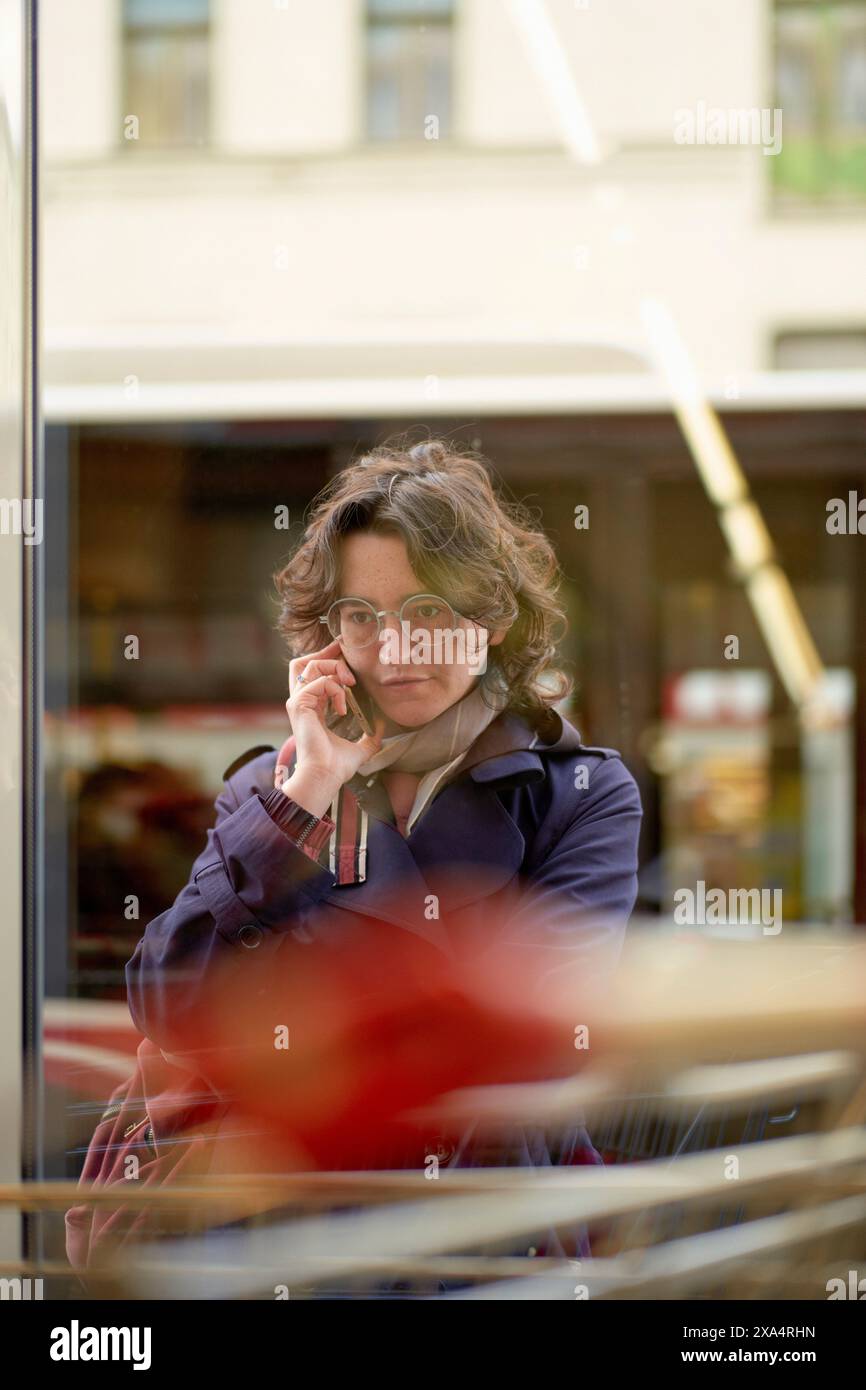 Femme parlant au téléphone à travers une fenêtre de café, profondément dans la pensée. Banque D'Images