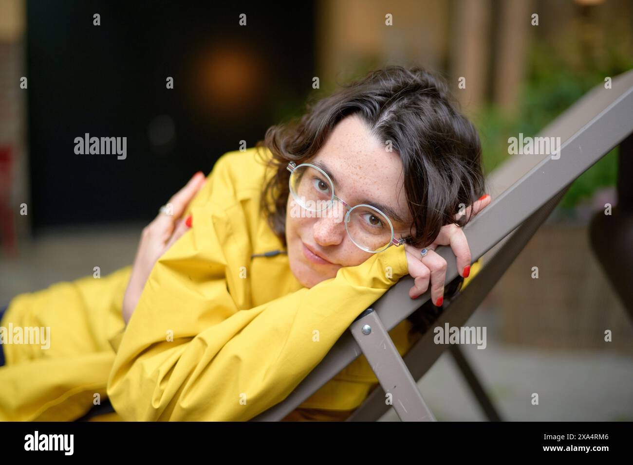 Femme souriante en veste jaune reposant sur une chaise Banque D'Images