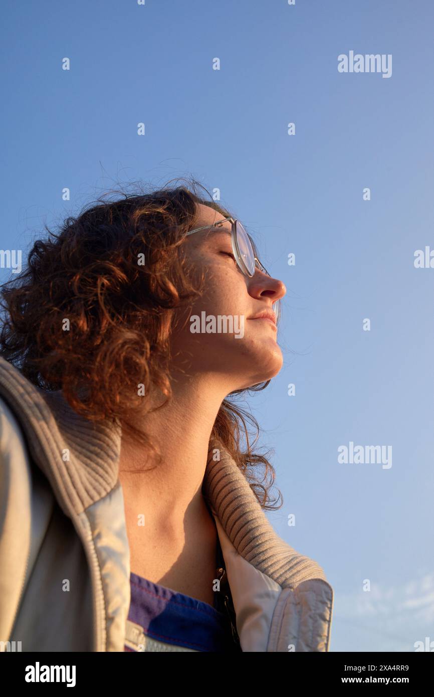 Jeune femme se prélassant dans la lueur chaude du ciel du coucher du soleil Banque D'Images