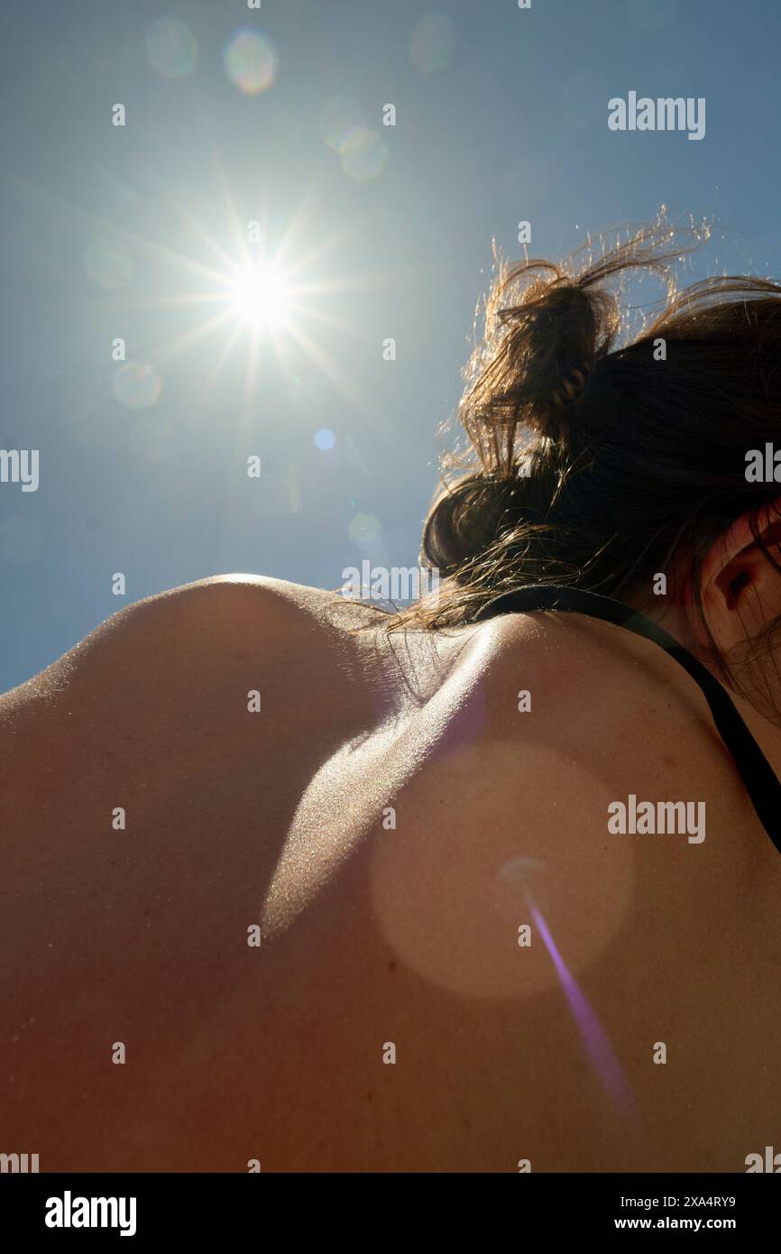 Vue arrière d'une personne avec la lumière du soleil qui brille sur son épaule, créant un effet de lumière parasite de lentille. Banque D'Images