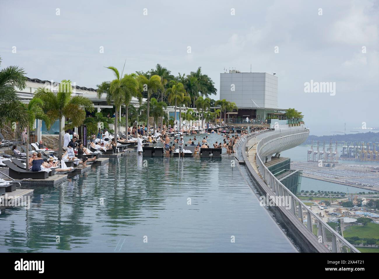 Piscine à débordement dans un complexe de luxe avec une ville pittoresque et la toile de fond de l'océan, avec des invités se prélasser et nager. Banque D'Images