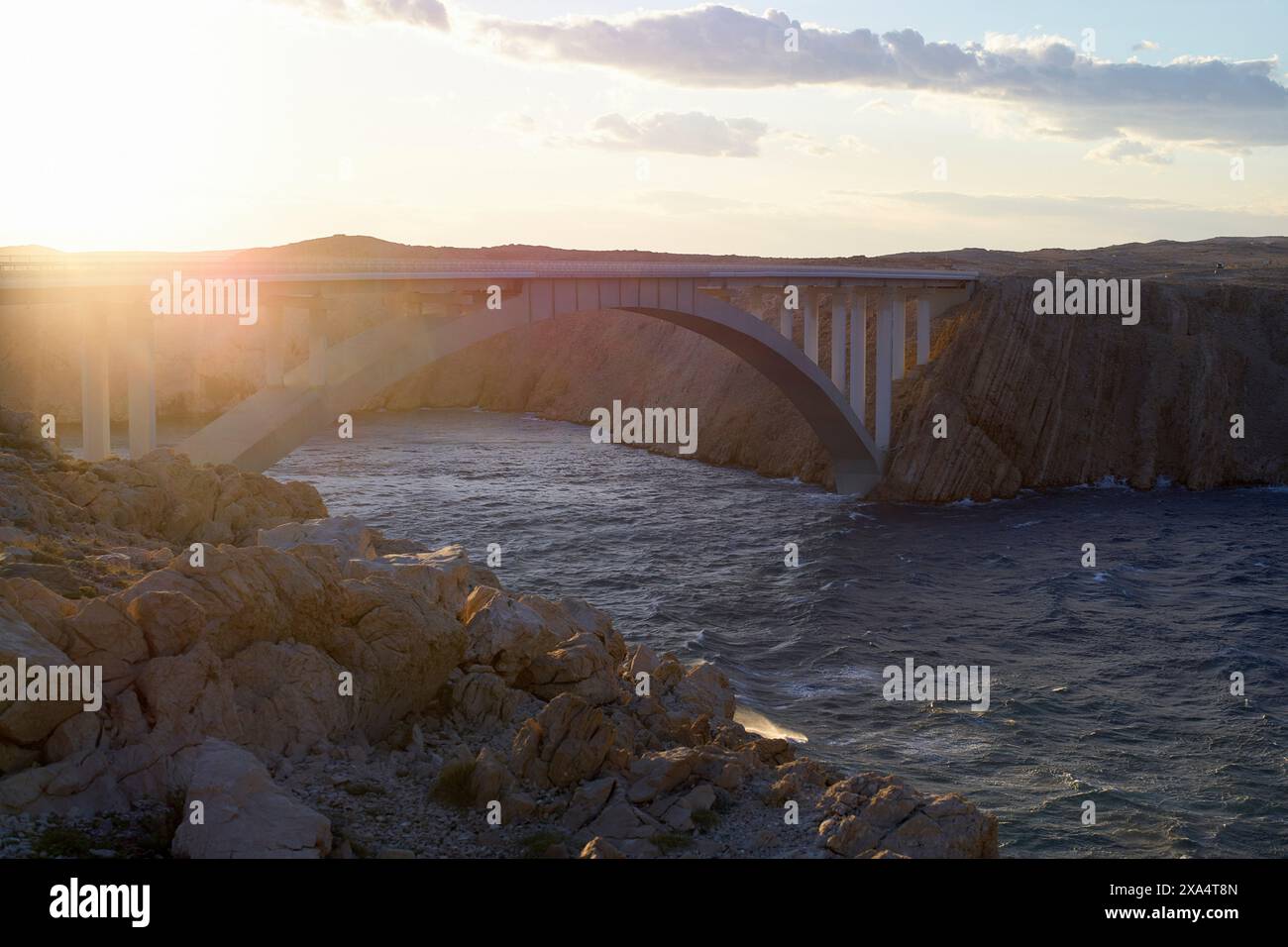 Lumière du coucher du soleil illuminant un pont voûté sur une rivière tranquille avec un terrain rocheux qui l'entoure. Banque D'Images