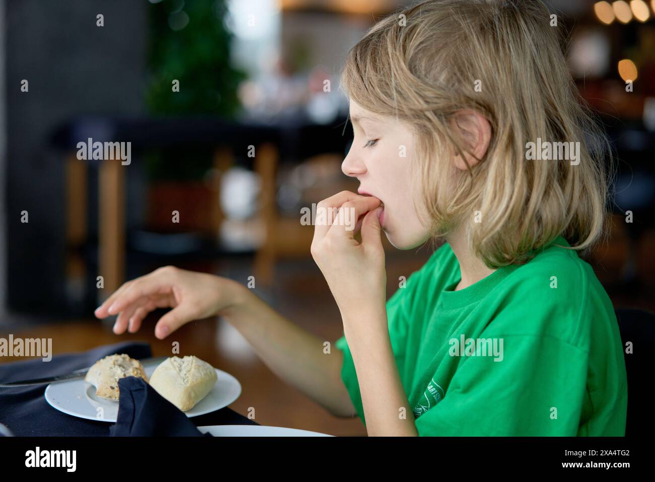 Jeune enfant dans une chemise verte dégustant de la nourriture à une table de restaurant. Banque D'Images