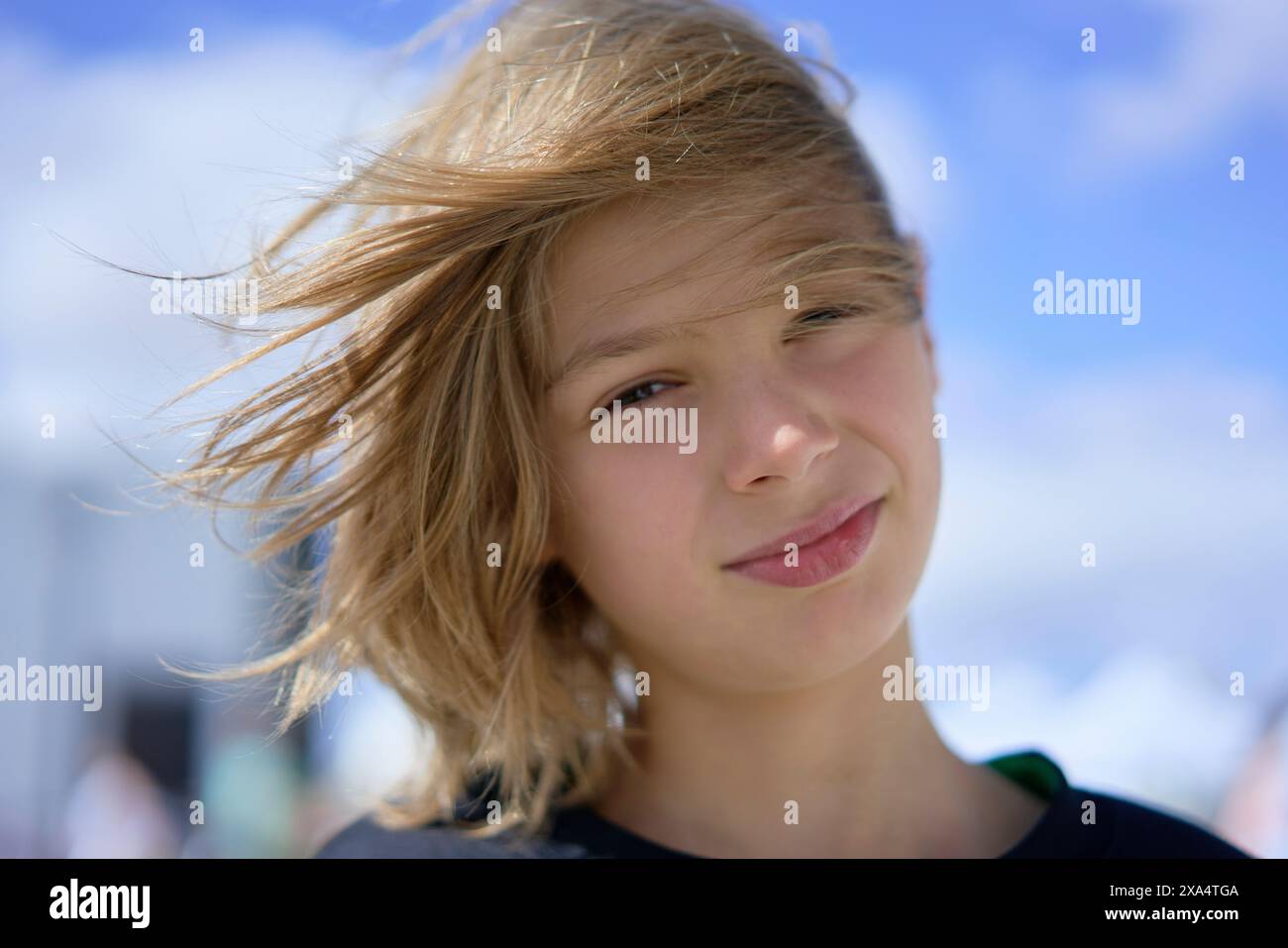 Jeune personne souriante avec les cheveux soufflés par le vent debout à l'extérieur par une journée ensoleillée. Banque D'Images