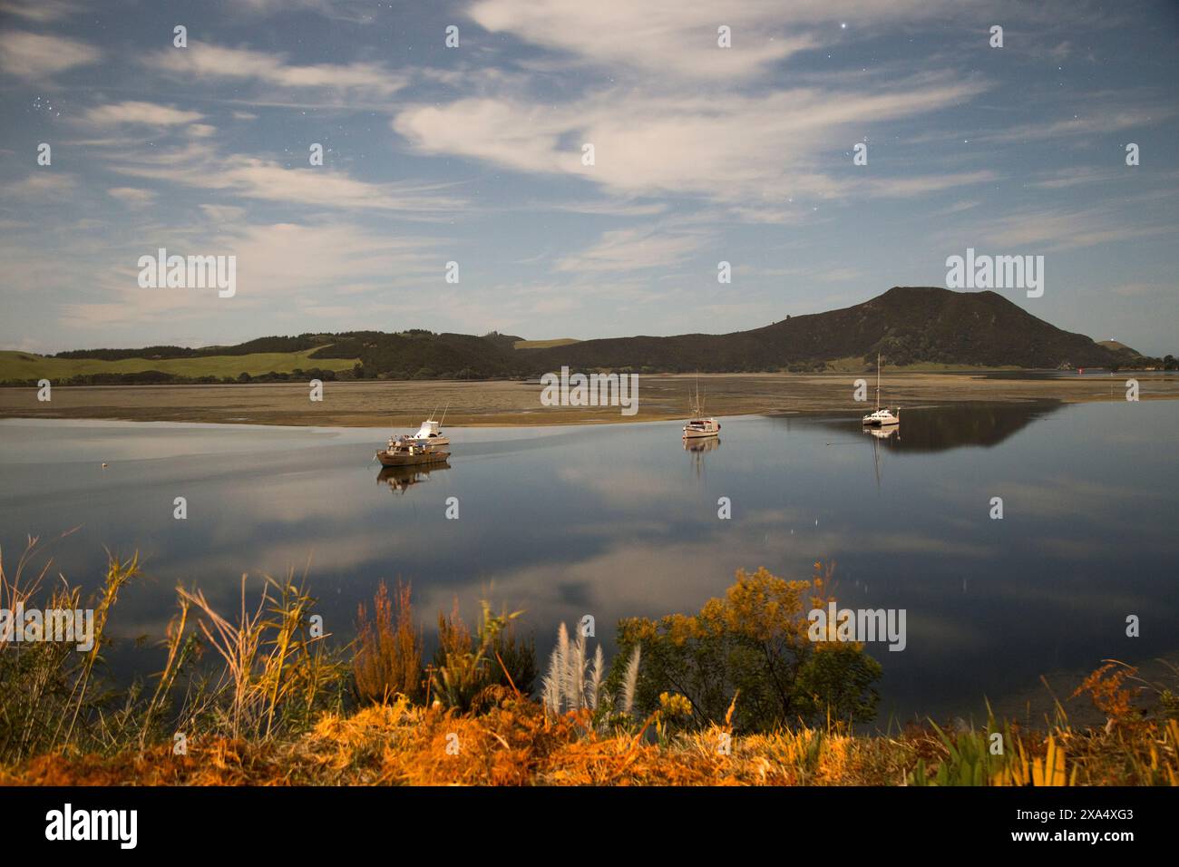 Paysage nocturne tranquille avec des bateaux ancrés sur un lac vitreux reflétant un ciel étoilé clair au-dessus et une montagne en arrière-plan. Banque D'Images