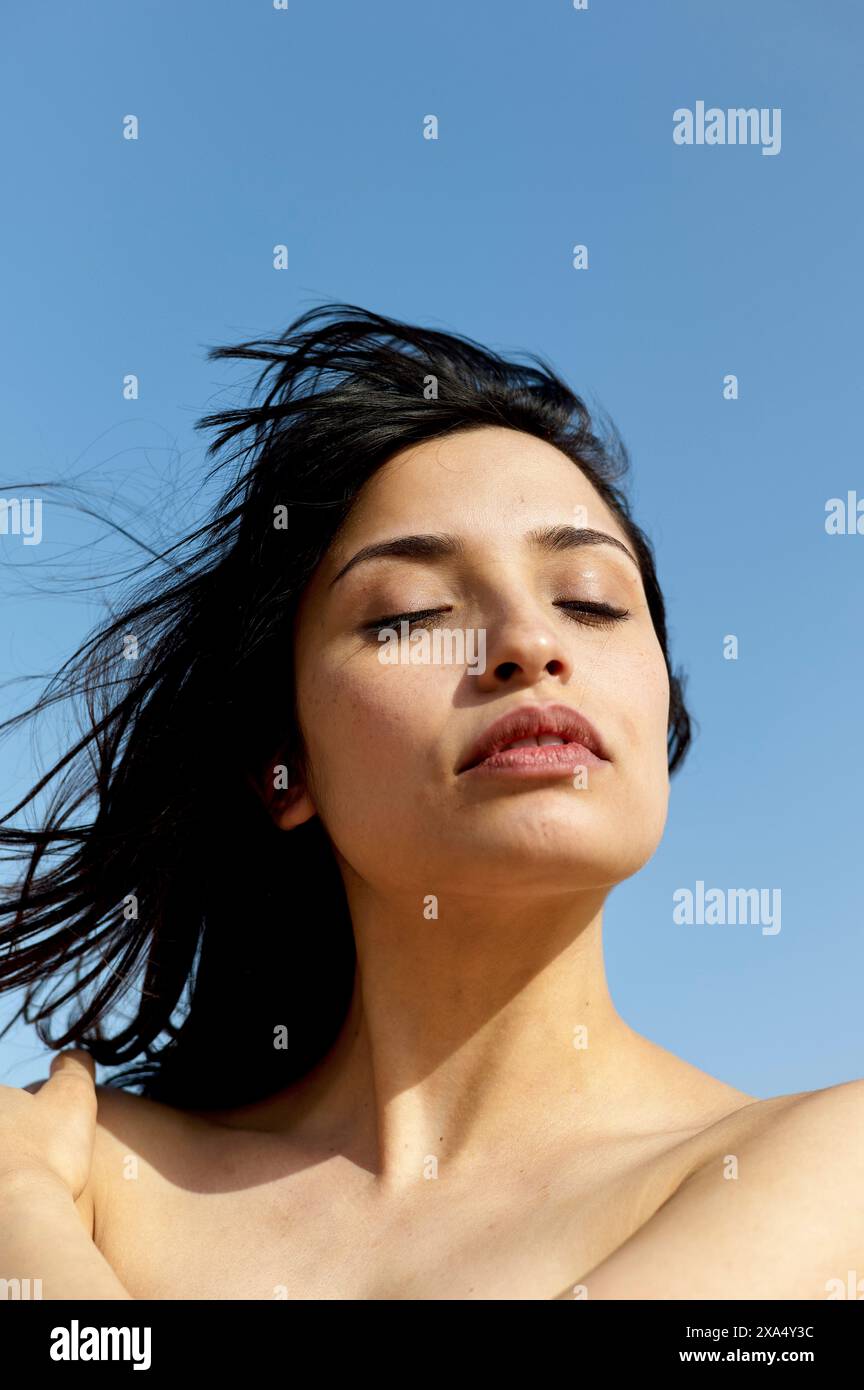 Une femme sereine aux cheveux foncés profite d'un moment de calme sous un ciel bleu clair. Banque D'Images