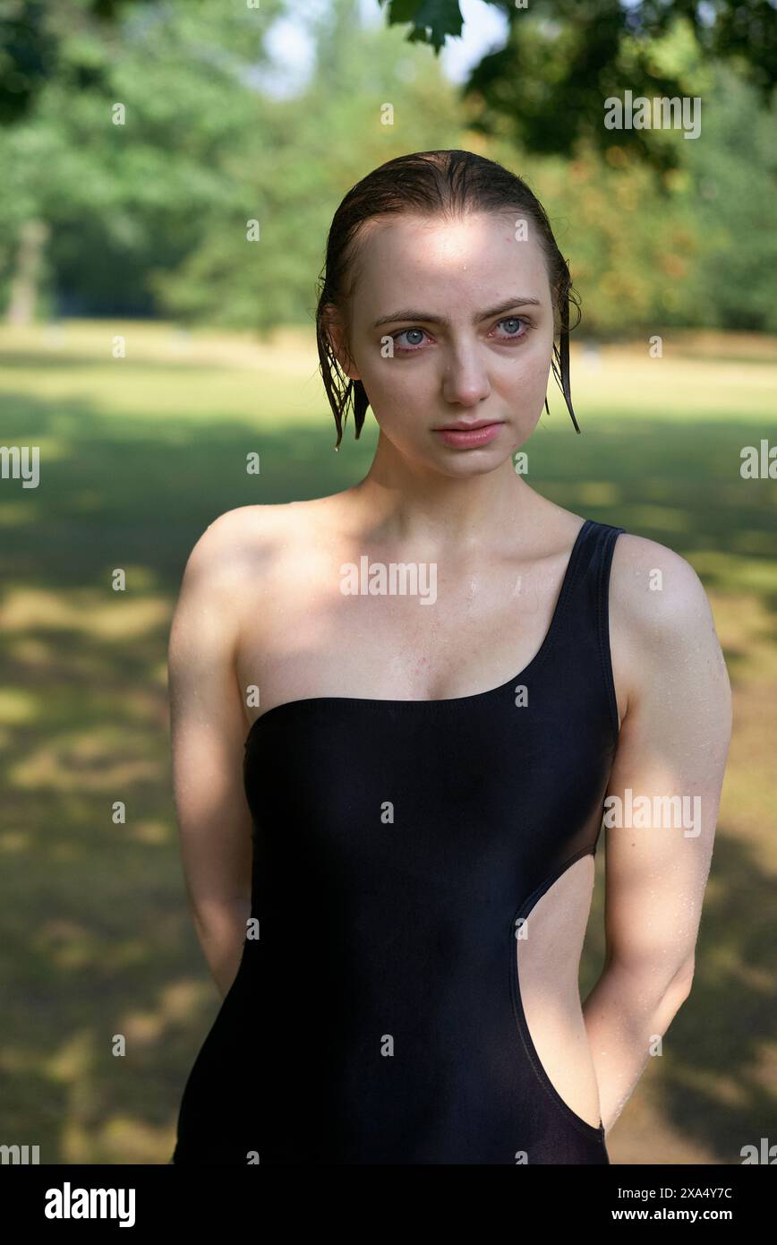 Femme confiante dans une robe noire se tient à l'extérieur avec les cheveux mouillés et une expression concentrée. Banque D'Images