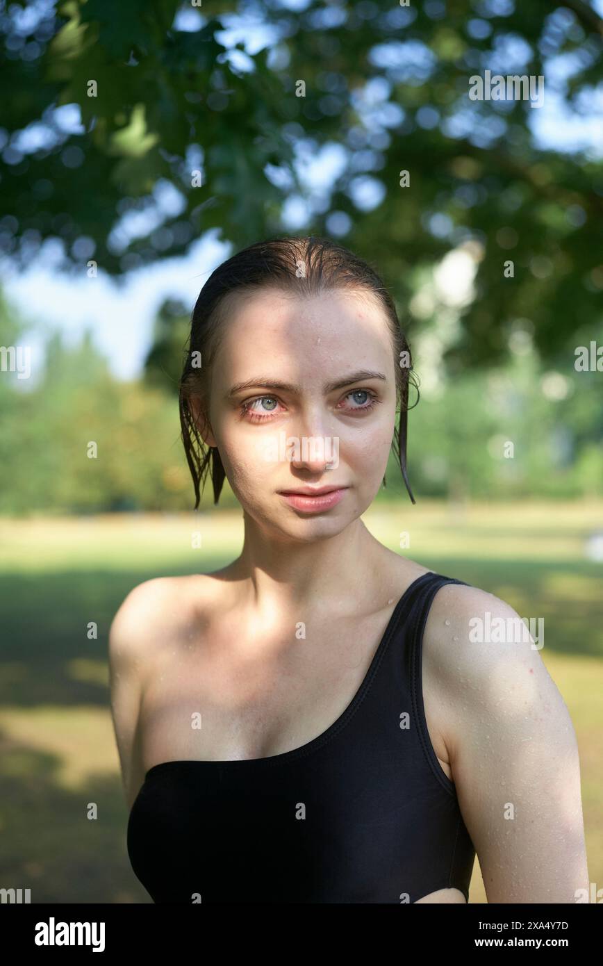 Femme dans un haut noir debout à l'extérieur avec des arbres en arrière-plan, regardant directement la caméra avec les yeux focalisés. Banque D'Images