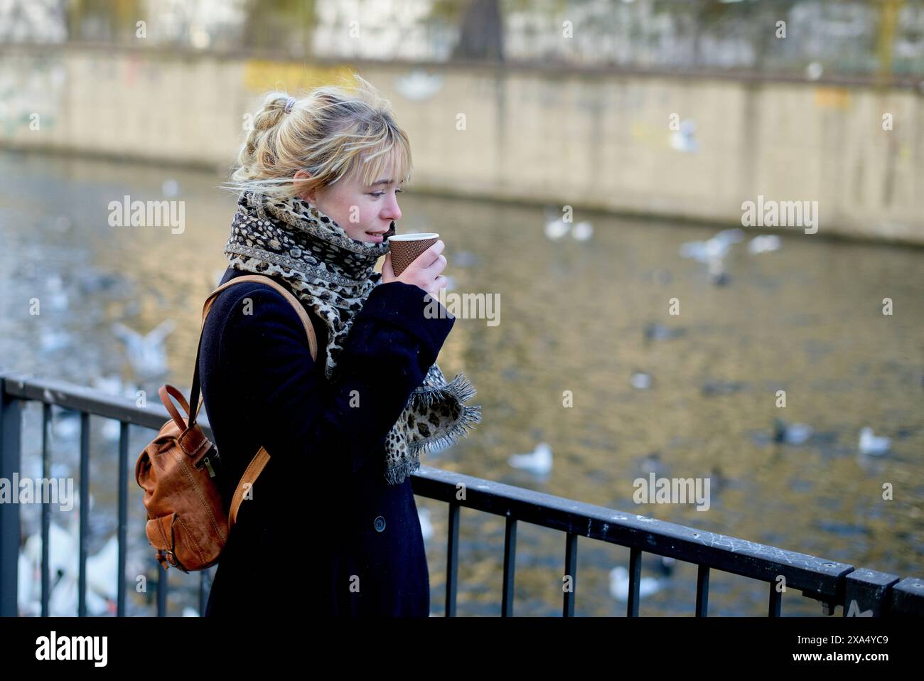 Femme profitant d'une boisson chaude par une rivière avec des oiseaux en arrière-plan par temps clair. Banque D'Images