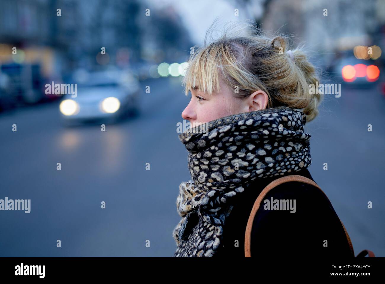 Profil latéral d'une femme blonde attendant au crépuscule avec des lumières de la ville en arrière-plan. Banque D'Images