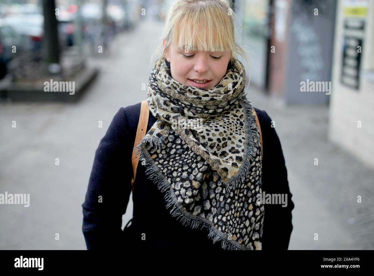Jeune femme souriante avec une frange blonde portant un foulard imprimé léopard et un manteau bleu marine dans une rue de la ville. Banque D'Images