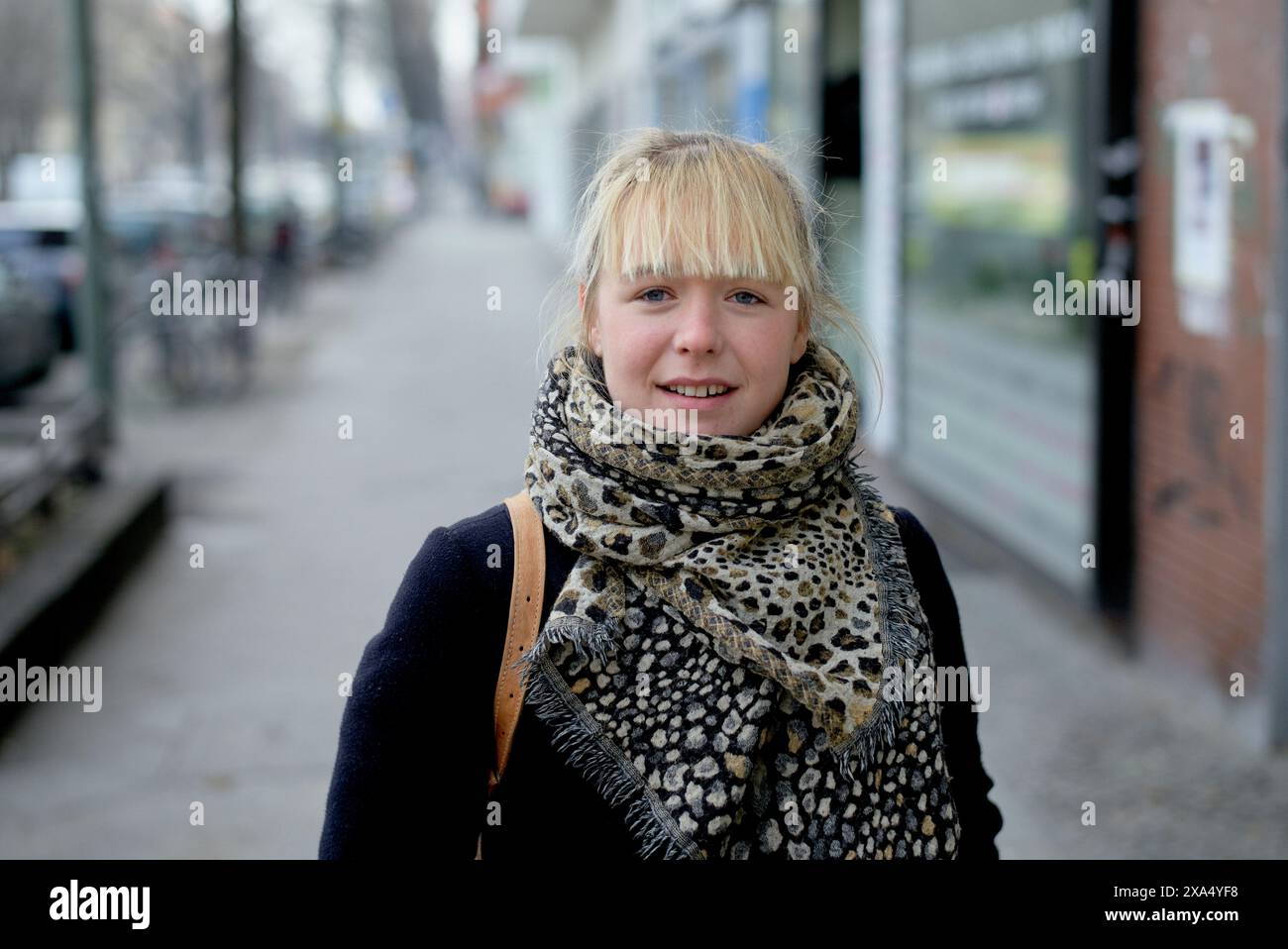 Jeune femme souriante avec des cheveux blonds et une écharpe à motifs debout sur un trottoir de la ville. Banque D'Images