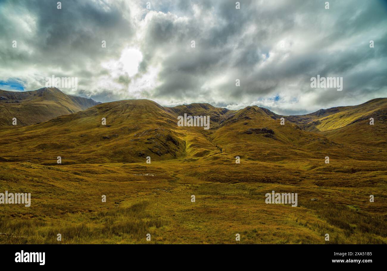 Vue spectaculaire sur les collines ondulantes sous un ciel nuageux avec des taches de soleil soulignant la texture du paysage. Banque D'Images