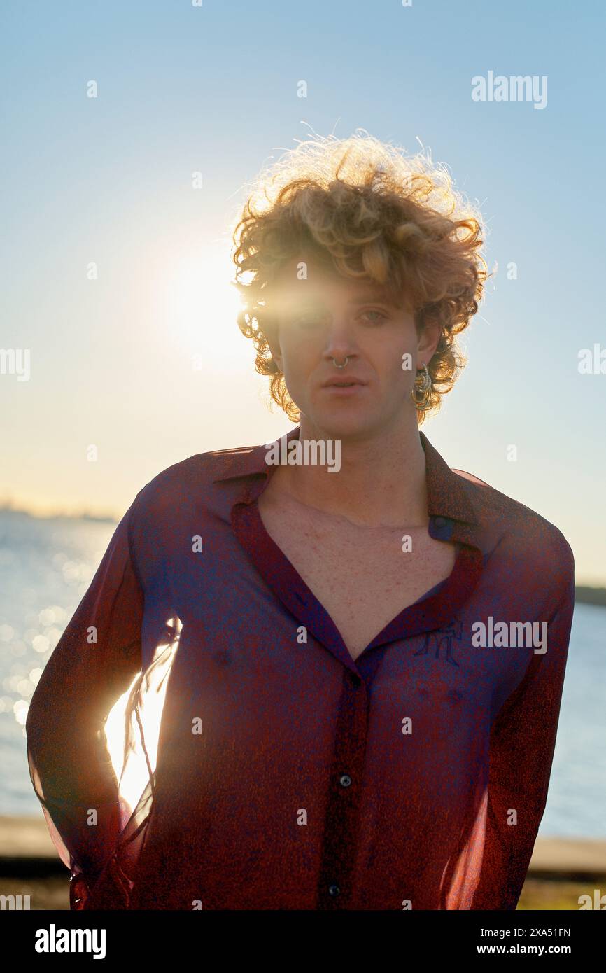 Silhouette ensoleillée d'une personne aux cheveux bouclés debout près de l'eau au coucher du soleil. Banque D'Images