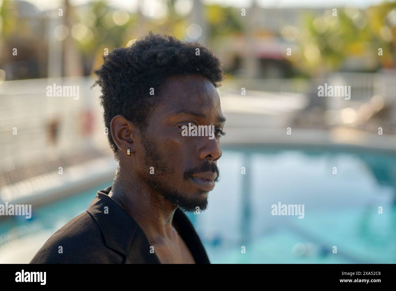 Gros plan d'un homme pensif avec une barbe debout près d'une piscine, avec son regard concentré hors caméra. Banque D'Images