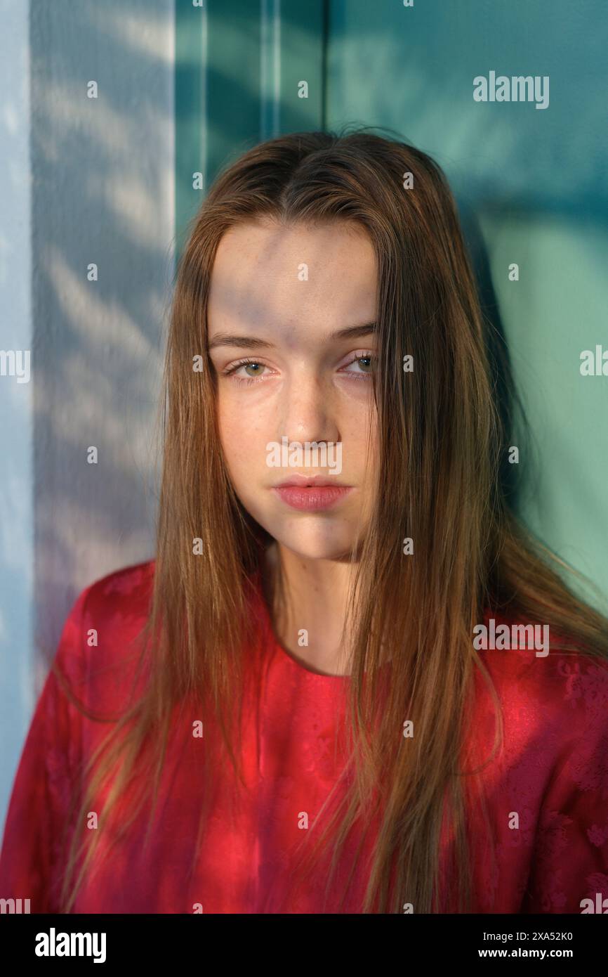 Jeune femme aux cheveux longs portant une chemise rouge debout devant une fenêtre en verre projetant une ombre sur son visage. Banque D'Images