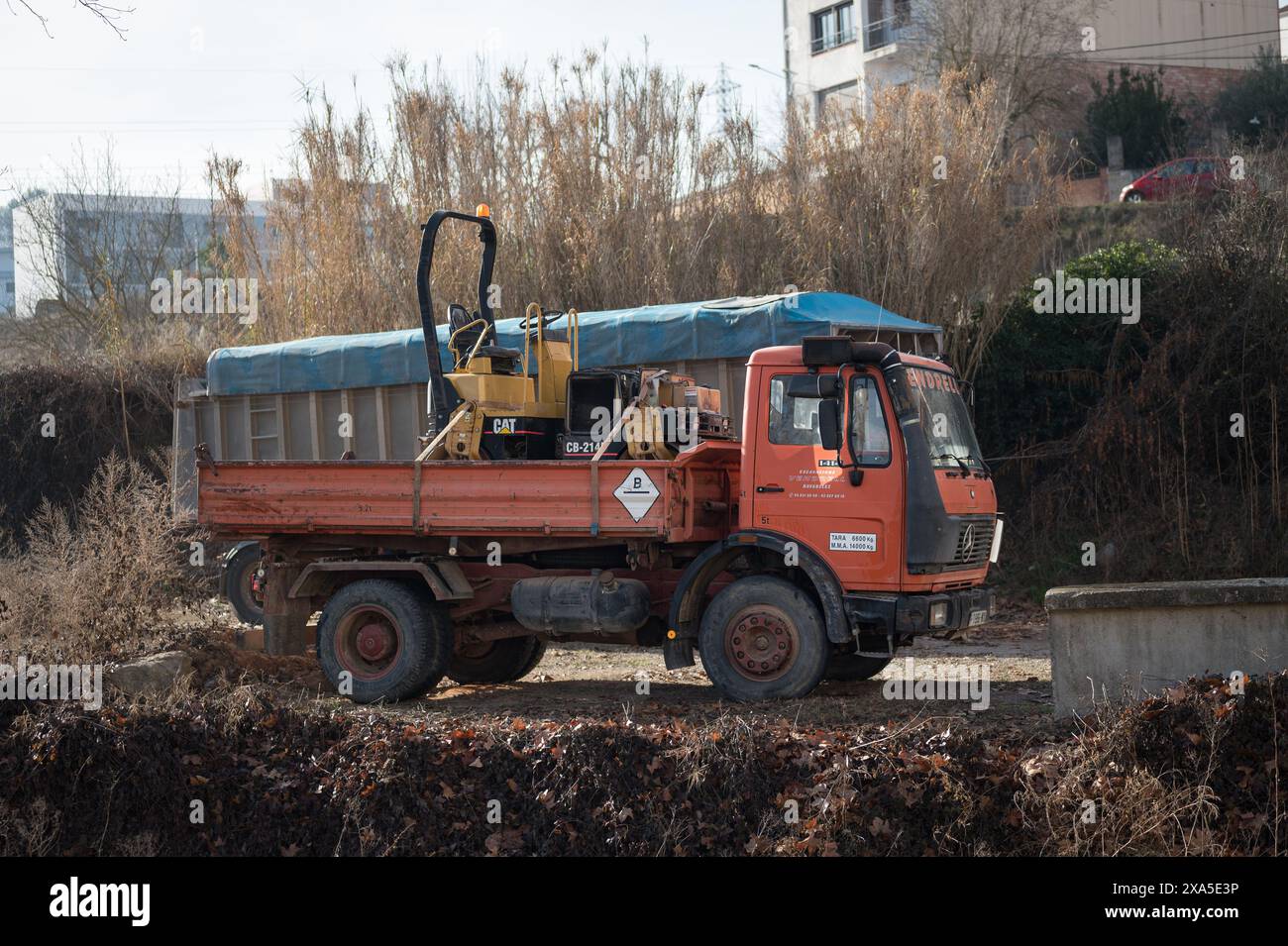 Vue latérale d'un camion de chantier Mercedes Benz 1414 orange chargeant un rouleau jaune Caterpillar CB-214. Banque D'Images