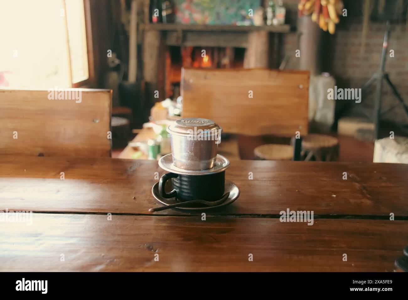 Café vietnamien traditionnel préparé par goutte à goutte lente sur une table en bois rustique avec une cheminée en pierre confortable allumée dans le fond flou Banque D'Images