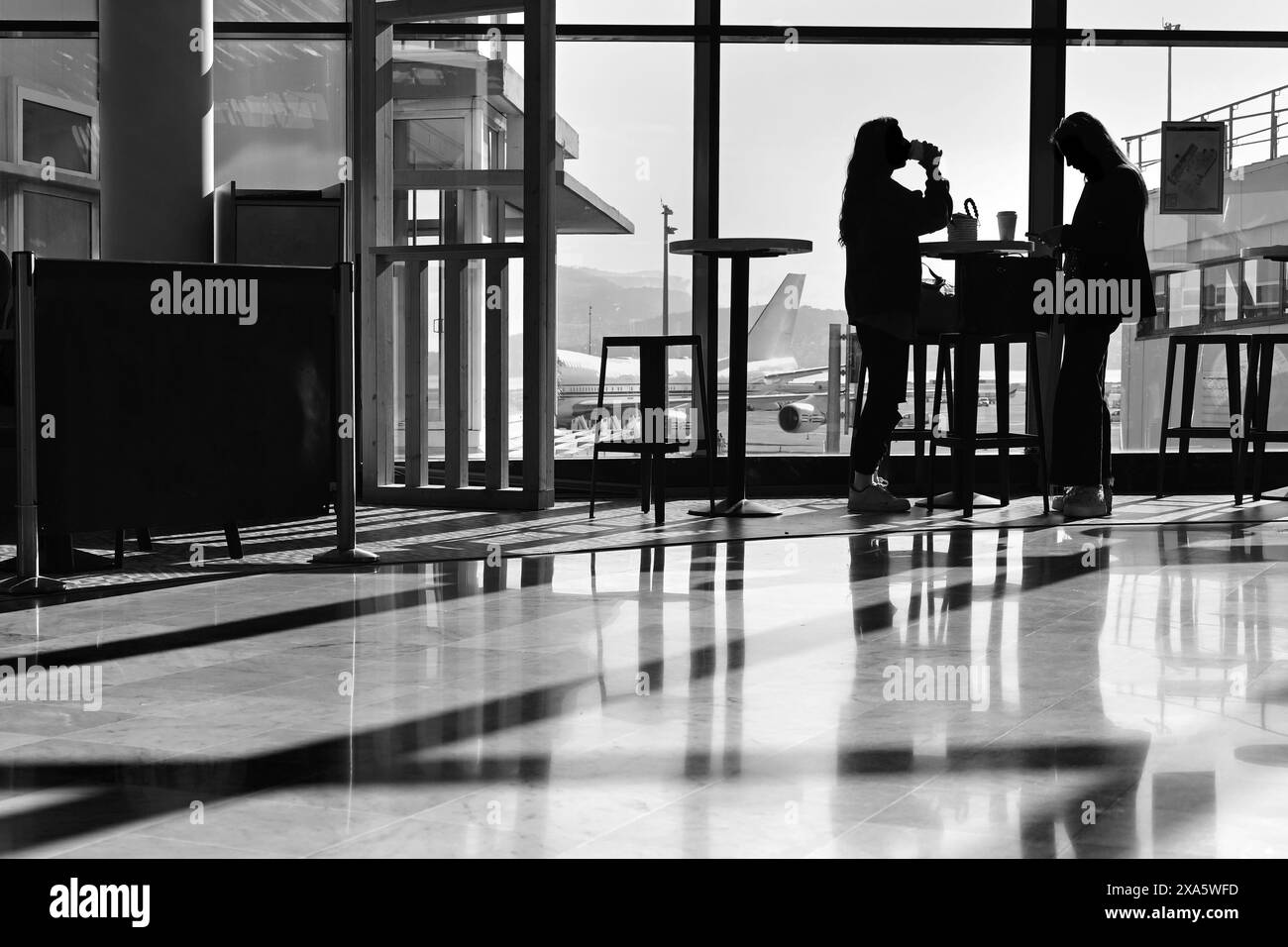 Aéroport Nice Côte d'azur, France, 21 mai 2024 : silhouettes de deux femmes debout près de la fenêtre dans la salle d'attente de l'aéroport en noir et blanc Banque D'Images