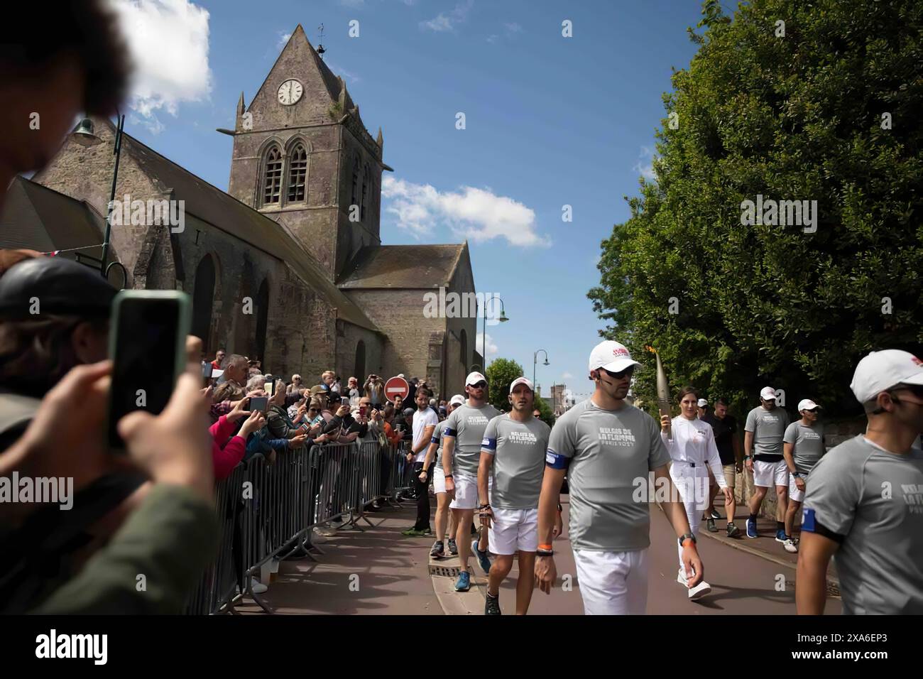 Une femme transporte la flamme olympique de Paris 2024 à travers la place de la ville de Sainte-mère-Église, en Normandie, dans le cadre du Relais de la flamme le 31 mai 2024. Les porteurs de flambeau ont marché dans le village alors que les célébrations avaient lieu avant le jour J 80. Des événements commémoratifs comme ceux-ci servent à honorer les sacrifices consentis par les membres du service américain il y a 80 ans pour assurer la paix et la sécurité, et inspirer les générations futures à valoriser une vision collective de la paix mondiale. Banque D'Images