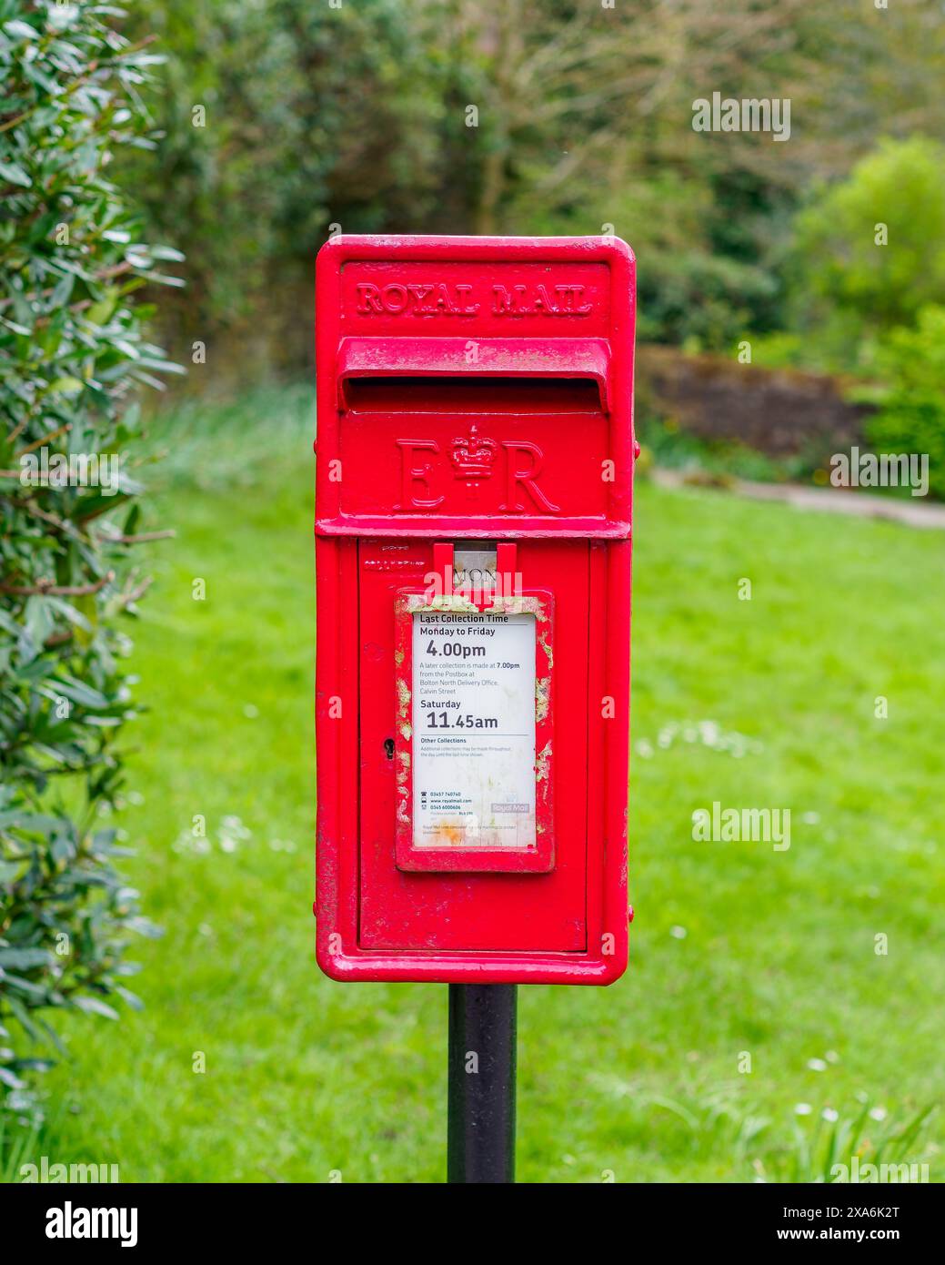 Une boîte postale royale rouge vue de face avec de l'herbe verte derrière dans un emplacement de campagne Banque D'Images