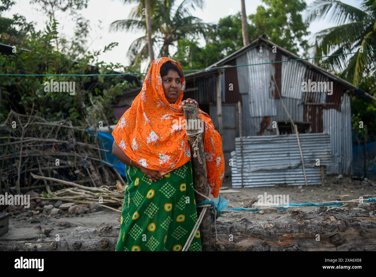 Une femme se tient debout dans une maison endommagée pendant les suites de la catastrophe à Mongla. Le cyclone Remal, qui a pris naissance dans la baie du Bengale, a frappé les districts côtiers du sud du Bangladesh dans la nuit du dimanche 26 mai. Le cyclone a entraîné des vents dévastateurs de 90 à 120 km/h, entraînant des inondations et des destructions considérables. Les Sundarbans, barrière naturelle critique et site du patrimoine mondial de l'UNESCO, ont subi le plus gros des conséquences du cyclone. Les eaux de crue ont fait un bond de trois à quatre pieds au-dessus de la normale, submergeant de vastes zones et causant des dommages importants à la faune et aux infrastructures, y compris le Karamjal Banque D'Images