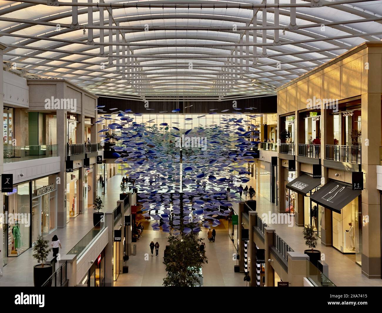 Atrium de centre commercial animé avec plafond de verre et beaucoup de gens marchent Banque D'Images