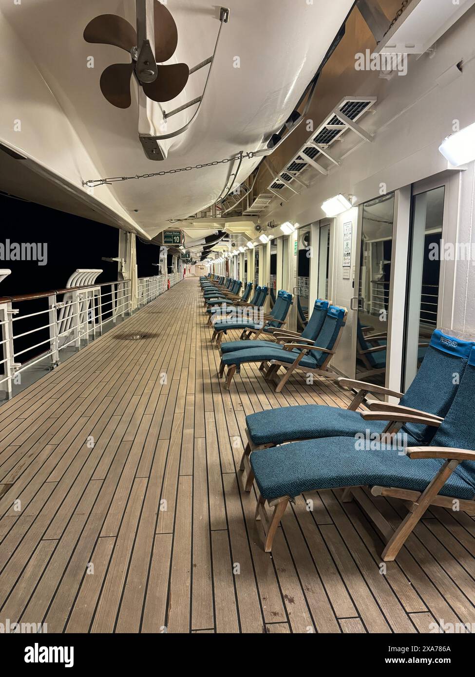 Chaises longues sur un pont de navire avec un ventilateur au plafond, fenêtres et portes derrière eux, pendant la nuit Banque D'Images