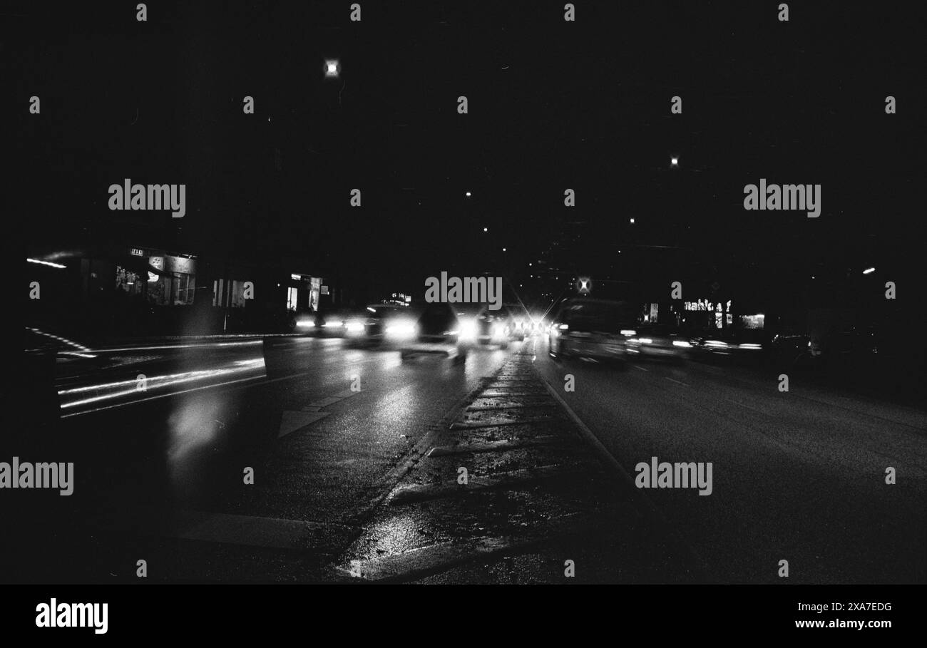 Une image monochrome de voitures conduisant dans une rue faiblement éclairée la nuit Banque D'Images