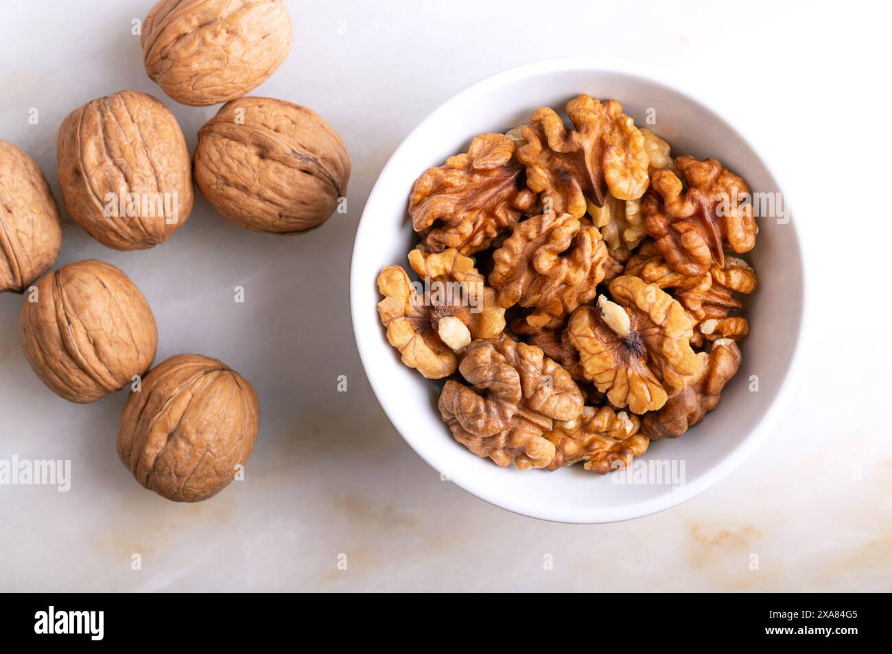 Noix dans un bol blanc sur une assiette en marbre. Moitiés décortiquées et séchées de cerneaux de noix, graines mûres du noyer commun Juglans regia. Banque D'Images