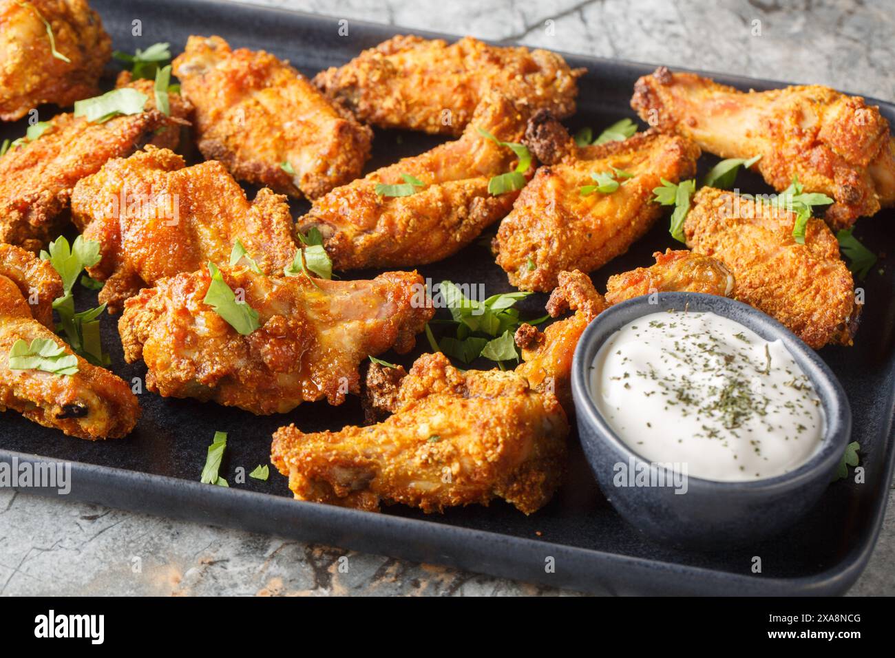 Savoureuses ailes de poulet au curry servies avec du yaourt grec en gros plan sur l'assiette sur la table en marbre. Horizontal Banque D'Images