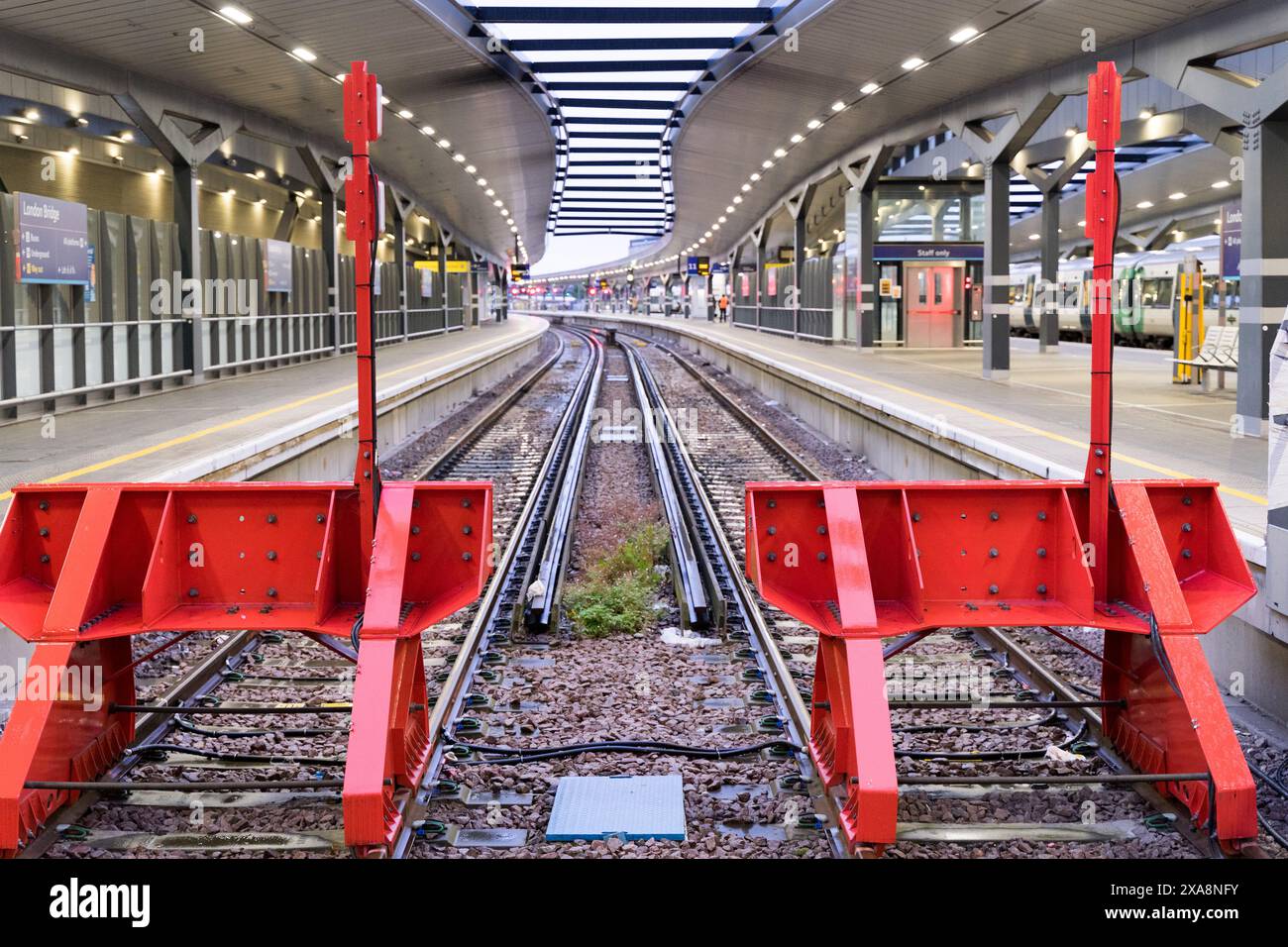 Deux arrêts tampons de train en rouge installés à l'extrémité de la plate-forme avec des voies vides éclairées par les projecteurs sur le toit de la plate-forme de la gare de Londres UK Banque D'Images
