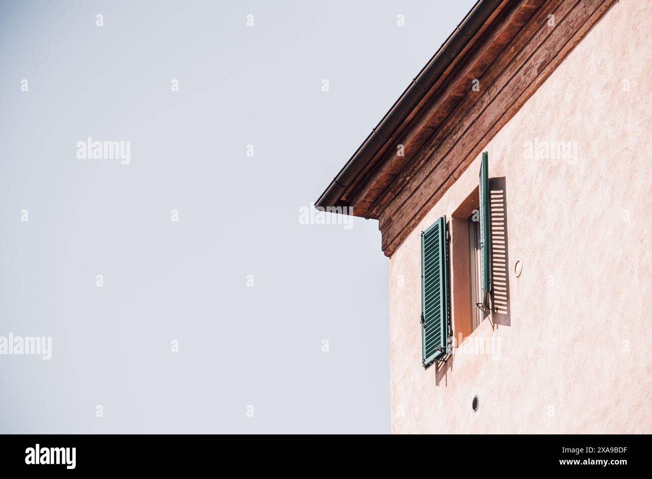 Ouvrez les volets verts sur une haute fenêtre d'une maison traditionnelle en Toscane, Italie par une journée ensoleillée avec une lumière vive et des ombres projetées sur le mur pâle. Banque D'Images