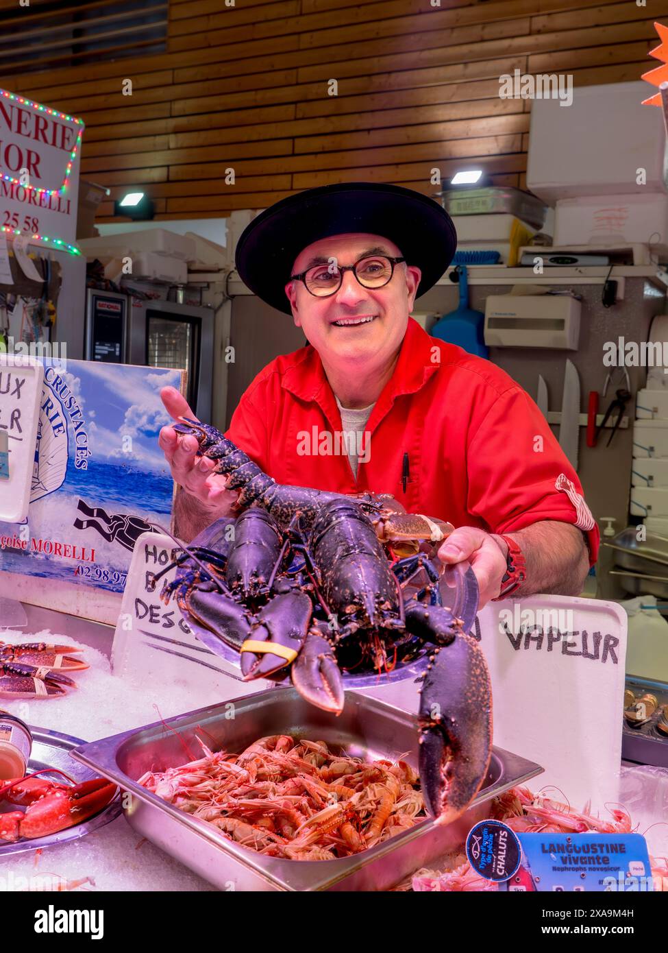 ÉTAL DE MARCHÉ AU HOMARD BLEU CONCARNEAU FRANCE BRETAGNE intérieur Concarneau halle de marché au poisson français et poissonnier de caractère, dans une tenue de style breton affichant fièrement son homard bleu vivant local à vendre Bretagne Finistère France Banque D'Images