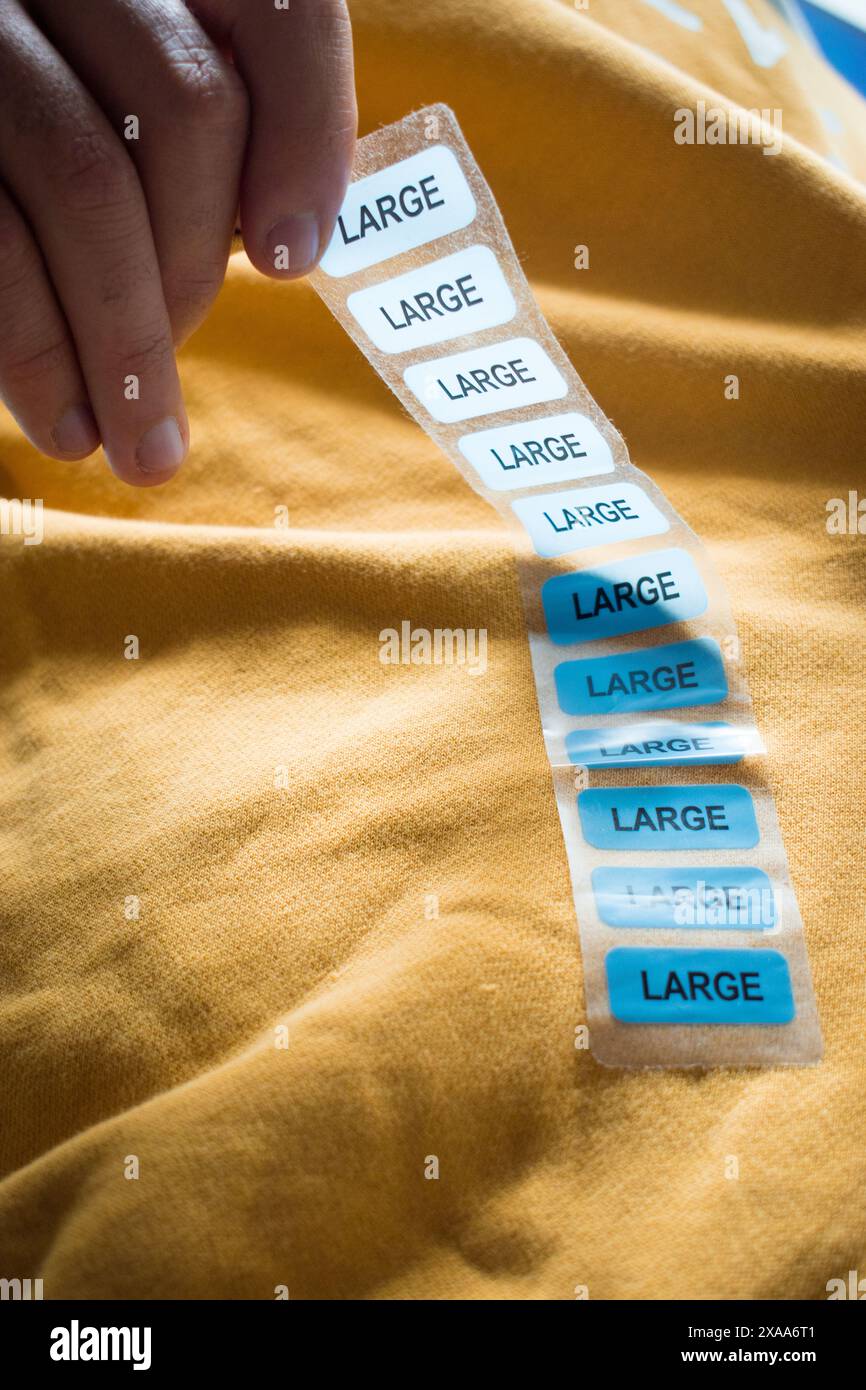 Une main tenant des étiquettes de grande taille au-dessus d'un chandail jaune Banque D'Images