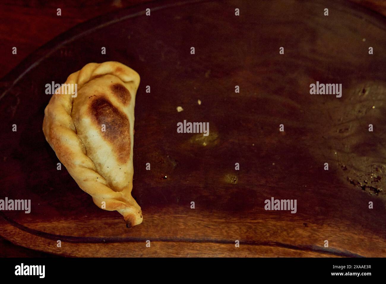 une seule empanada salteña sur une planche de bois. Nourriture typique du nord de l'Argentine. Banque D'Images