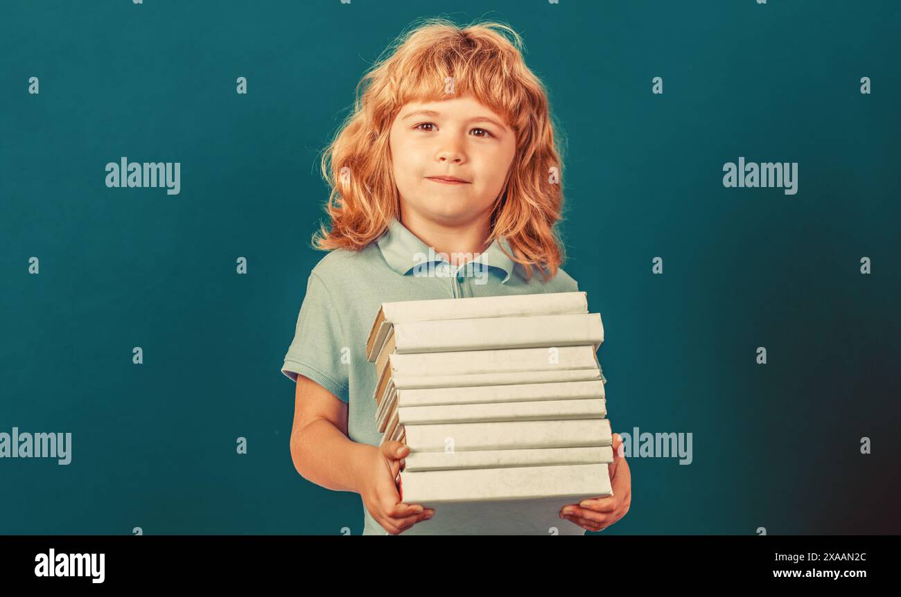 Heureux écolier avec des livres près du tableau noir. Retour à l'école. Écolier en classe. Enfant tenant pile de livres avec tableau de mortier sur tableau noir Banque D'Images