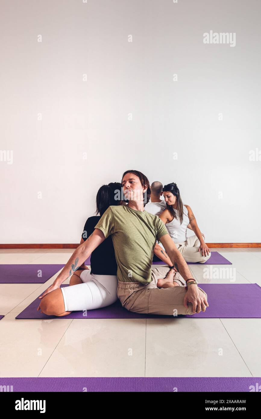 Groupe de personnes dans un cours de yoga faisant des postures par paires tout en étant assis sur un tapis dans le gymnase. Format vertical avec espace de copie. Banque D'Images